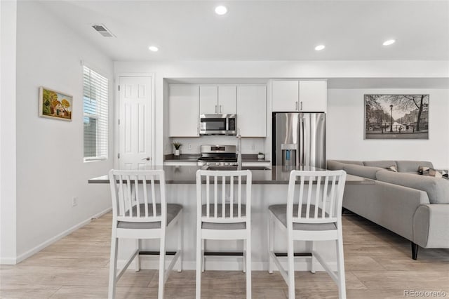 kitchen with light wood finished floors, a kitchen bar, dark countertops, visible vents, and appliances with stainless steel finishes