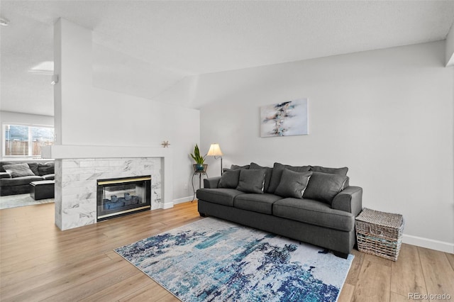 living room featuring a high end fireplace, vaulted ceiling, and hardwood / wood-style flooring