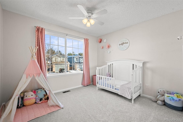 carpeted bedroom with ceiling fan, a crib, and a textured ceiling