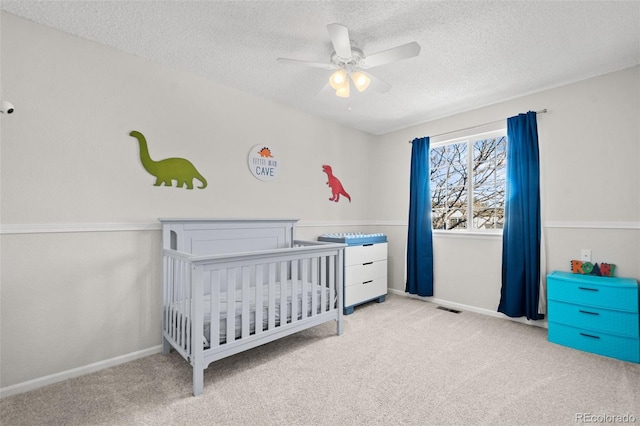 carpeted bedroom featuring a textured ceiling, ceiling fan, and a crib