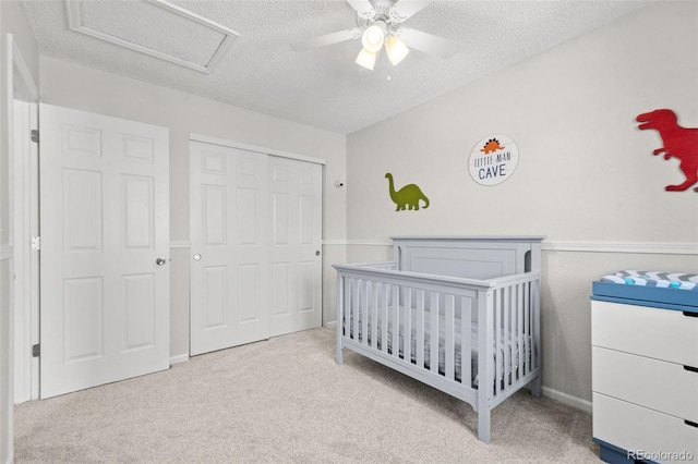 carpeted bedroom with a textured ceiling, ceiling fan, a closet, and a crib