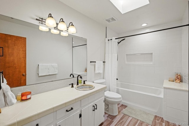 full bathroom featuring vanity, hardwood / wood-style floors, toilet, shower / tub combo with curtain, and a skylight