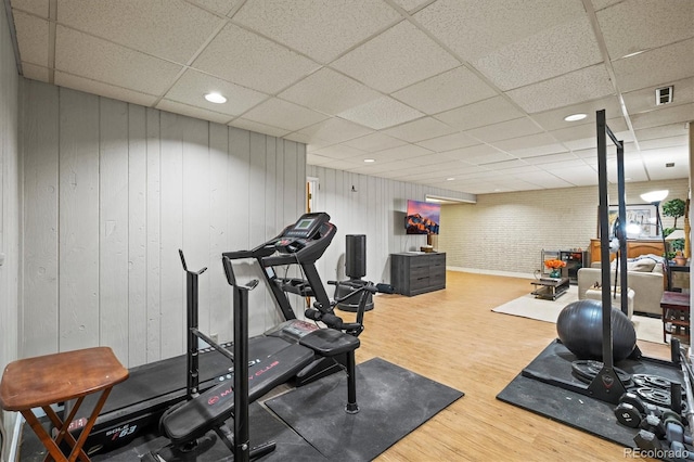 exercise area featuring wooden walls, a drop ceiling, and wood-type flooring