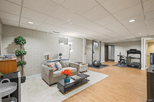 living room featuring a drop ceiling, wood-type flooring, and brick wall