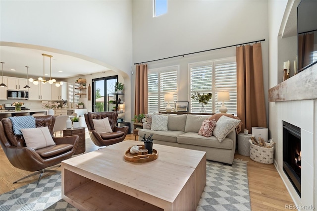 7853 S Jasper Way, Englewood, CO 80112 - living area with arched walkways, light wood-style floors, a warm lit fireplace, a towering ceiling, and a chandelier