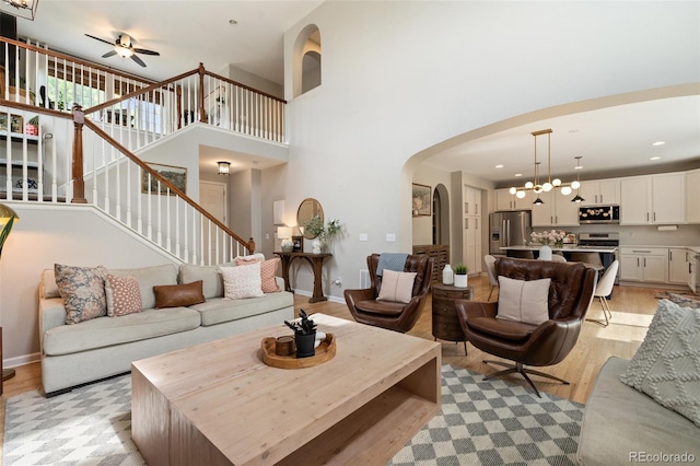 7853 S Jasper Way, Englewood, CO 80112 - living room featuring arched walkways, a ceiling fan, a chandelier, light wood finished floors, and a towering ceiling