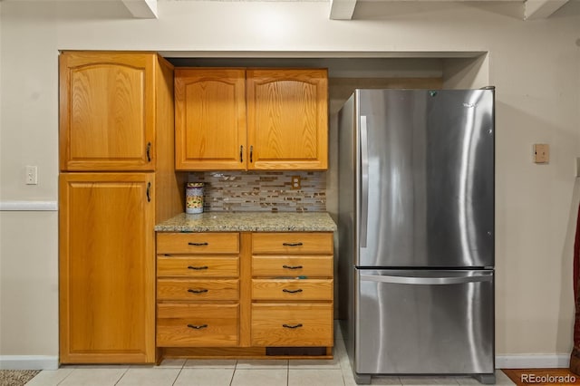 7260 Otis Ct, Arvada, CO 80003 - kitchen with freestanding refrigerator, tasteful backsplash, light tile patterned flooring, light stone counters, and brown cabinets