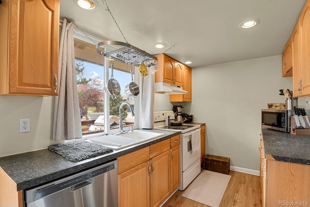 kitchen featuring a sink, dark countertops, stainless steel appliances, under cabinet range hood, and light wood-style floors