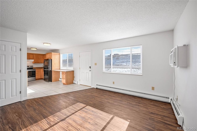 unfurnished living room featuring a wall mounted air conditioner, a baseboard radiator, a textured ceiling, and light wood-type flooring