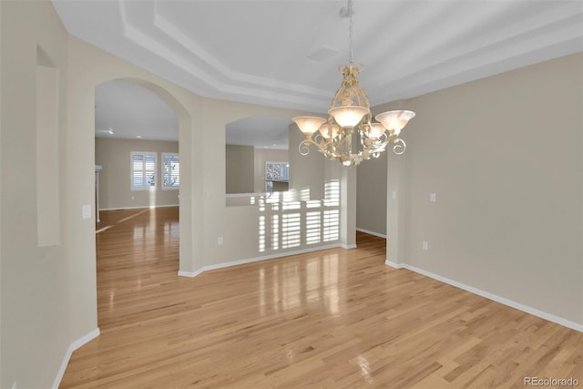 unfurnished dining area featuring a chandelier, light wood-type flooring, and a tray ceiling