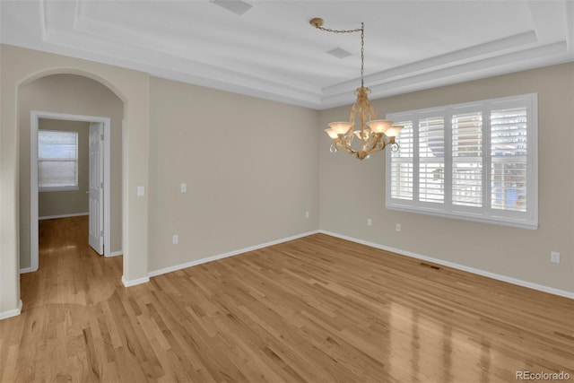 empty room with a notable chandelier, light hardwood / wood-style flooring, and a raised ceiling