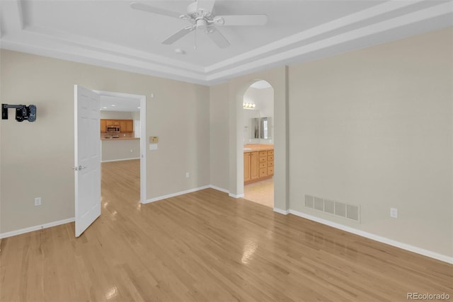 empty room with ceiling fan, a tray ceiling, and light hardwood / wood-style floors