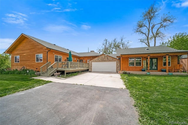 log home featuring an attached garage, a front yard, covered porch, an outbuilding, and driveway