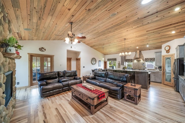 living area with high vaulted ceiling, light wood-style flooring, ceiling fan with notable chandelier, a stone fireplace, and wooden ceiling