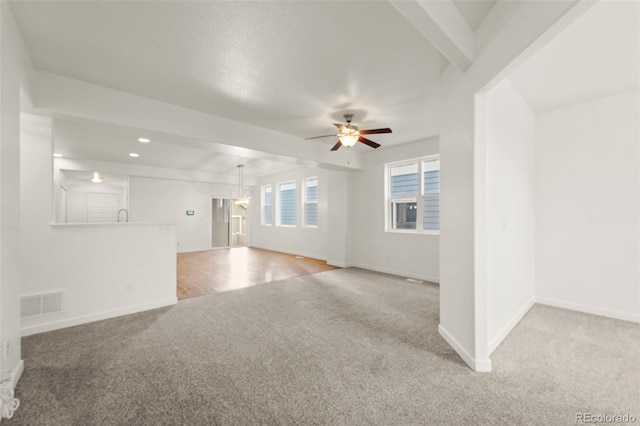 unfurnished living room with beamed ceiling, ceiling fan, and light carpet