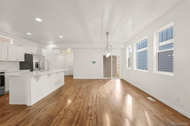 kitchen featuring appliances with stainless steel finishes, a kitchen island with sink, wood-type flooring, decorative light fixtures, and white cabinetry