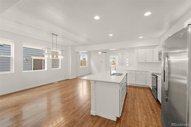 kitchen with white cabinets, sink, an island with sink, wood-type flooring, and stainless steel appliances