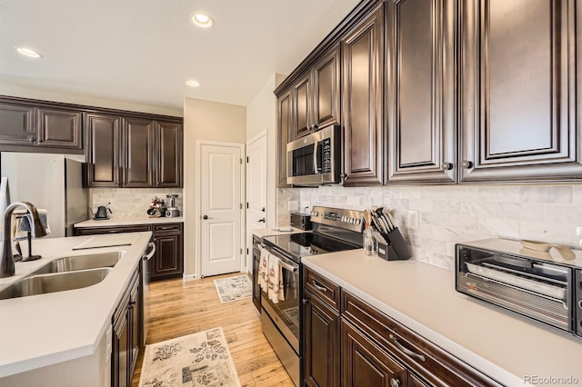 kitchen with a sink, light wood finished floors, light countertops, stainless steel appliances, and decorative backsplash