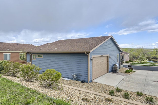 view of side of home featuring a garage, roof with shingles, and driveway