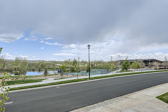 view of road featuring street lighting, a water view, sidewalks, and curbs