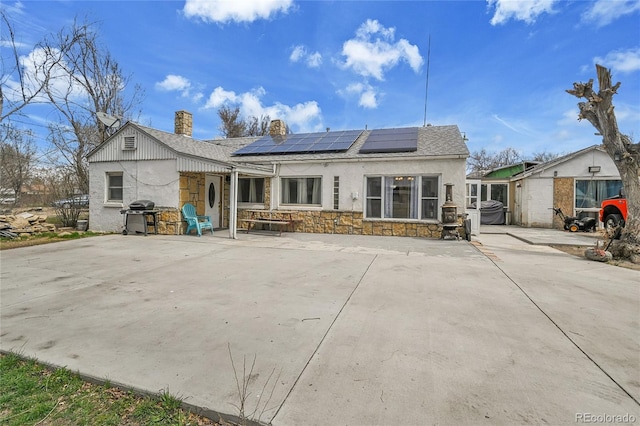 rear view of property with stone siding, a patio, a chimney, solar panels, and stucco siding