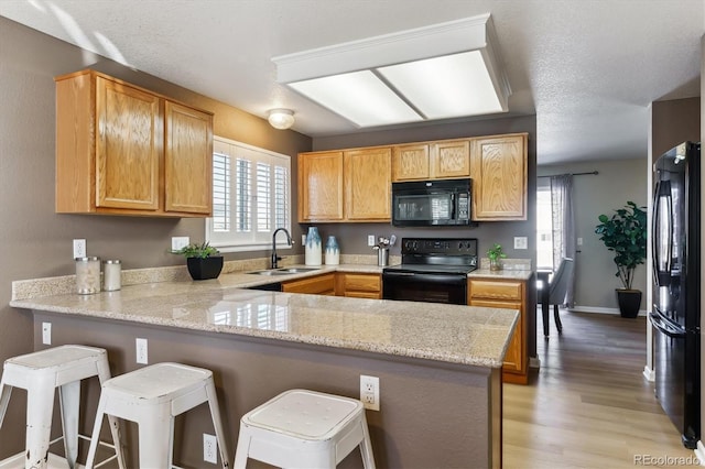 kitchen featuring sink, a breakfast bar area, light stone counters, black appliances, and kitchen peninsula