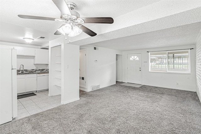 unfurnished living room with ceiling fan, a textured ceiling, sink, and light colored carpet