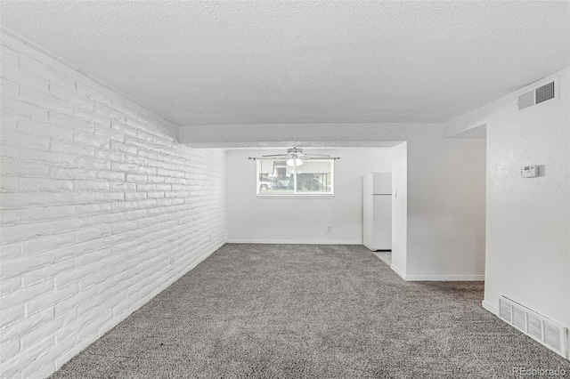 unfurnished room featuring ceiling fan, brick wall, a textured ceiling, and carpet floors