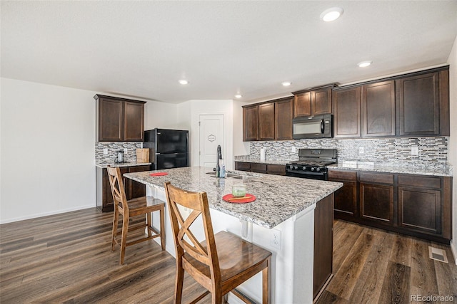 kitchen with a breakfast bar, black appliances, a center island with sink, sink, and light stone countertops