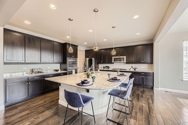 kitchen with appliances with stainless steel finishes, dark wood finished floors, a breakfast bar area, dark brown cabinets, and recessed lighting