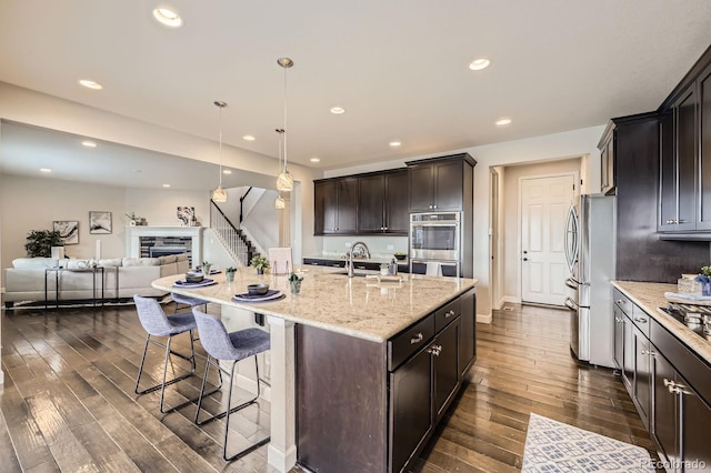 kitchen with stainless steel appliances, open floor plan, a sink, dark wood-type flooring, and a kitchen bar