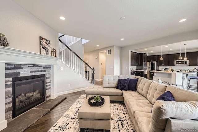 living room featuring hardwood / wood-style floors, stairs, a stone fireplace, recessed lighting, and baseboards