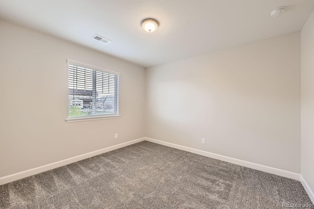 empty room featuring dark colored carpet, a smoke detector, and baseboards