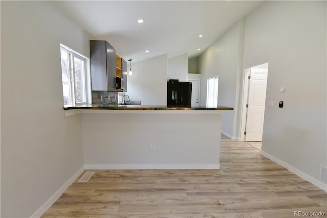 kitchen featuring kitchen peninsula, tasteful backsplash, black fridge, high vaulted ceiling, and light hardwood / wood-style floors