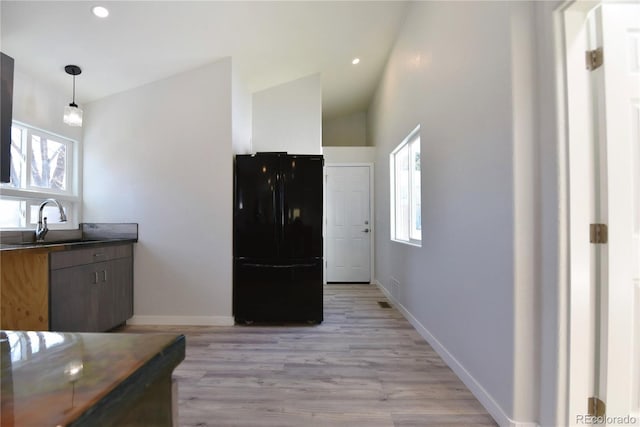 kitchen featuring sink, lofted ceiling, decorative light fixtures, black refrigerator, and light wood-type flooring