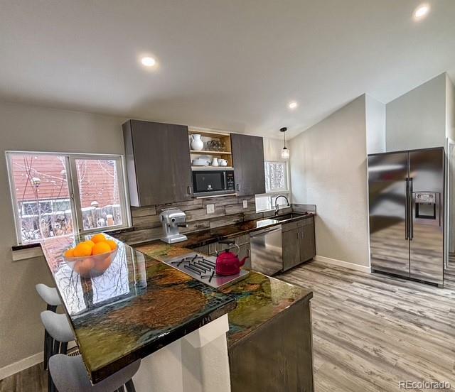 kitchen with light wood-type flooring, decorative light fixtures, black fridge with ice dispenser, stainless steel dishwasher, and dark brown cabinets