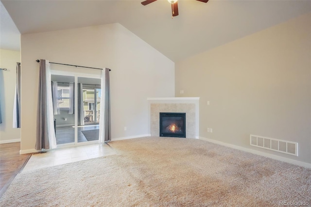 unfurnished living room with ceiling fan, light colored carpet, a tiled fireplace, and high vaulted ceiling