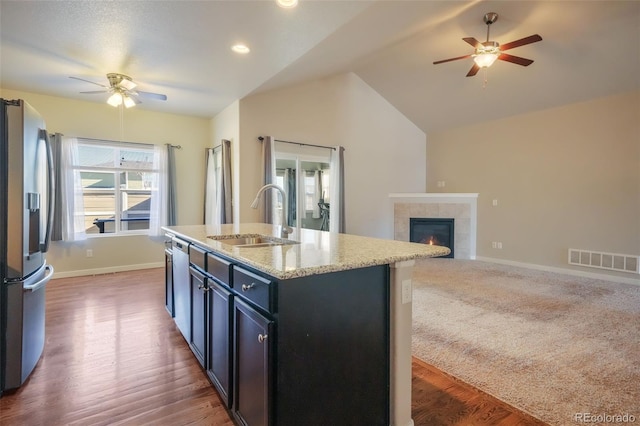 kitchen featuring appliances with stainless steel finishes, lofted ceiling, sink, a tile fireplace, and a center island with sink