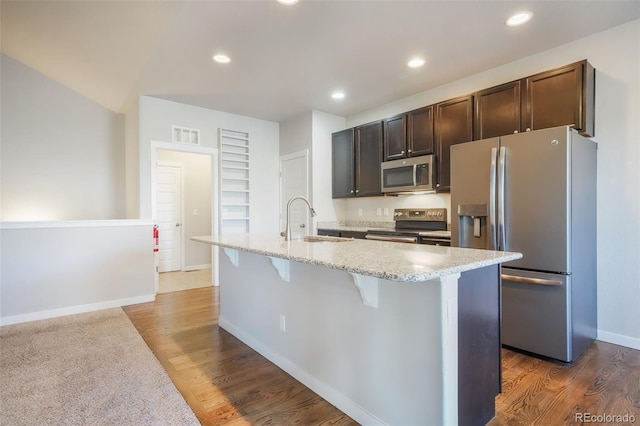 kitchen with a kitchen bar, dark wood-type flooring, stainless steel appliances, an island with sink, and sink