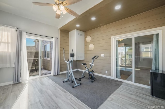 exercise room featuring light hardwood / wood-style floors, ceiling fan, and wooden walls