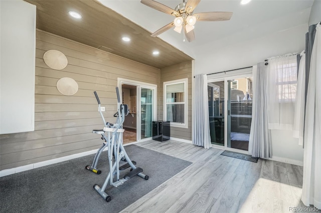 exercise room with ceiling fan, light wood-type flooring, and wooden walls