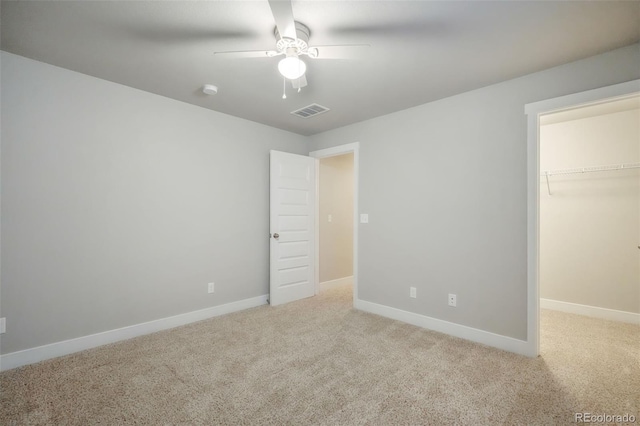 unfurnished bedroom with light carpet, ceiling fan, a walk in closet, and a closet