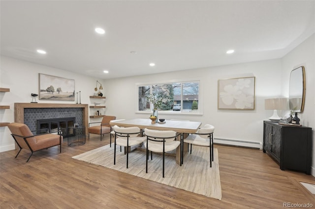 dining room with a fireplace, baseboard heating, wood finished floors, and recessed lighting