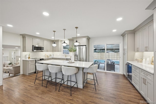 kitchen with appliances with stainless steel finishes, wine cooler, dark wood-type flooring, and a breakfast bar