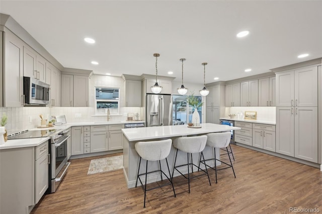 kitchen featuring a breakfast bar area, wood finished floors, stainless steel appliances, gray cabinetry, and a sink