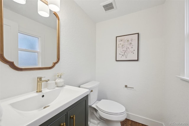 half bathroom featuring visible vents, toilet, vanity, wood finished floors, and baseboards