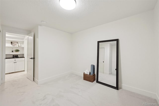 interior space with light colored carpet, a textured ceiling, and baseboards