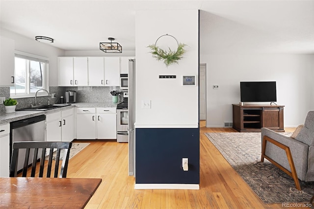 kitchen with sink, light hardwood / wood-style flooring, appliances with stainless steel finishes, tasteful backsplash, and white cabinets