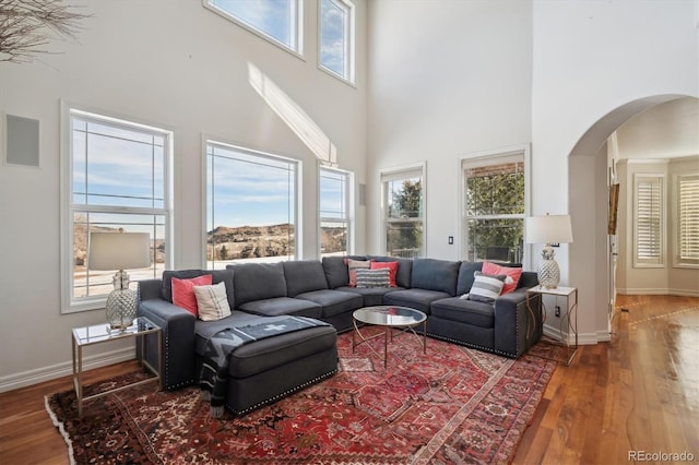 living room with arched walkways, a towering ceiling, baseboards, and wood finished floors