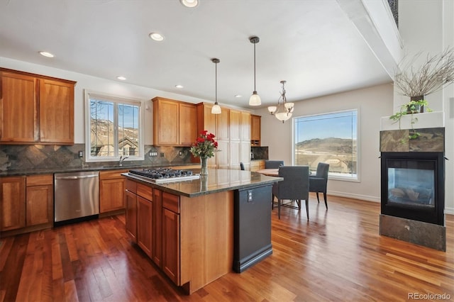 kitchen with dark wood-type flooring, a kitchen island, appliances with stainless steel finishes, dark stone countertops, and decorative light fixtures